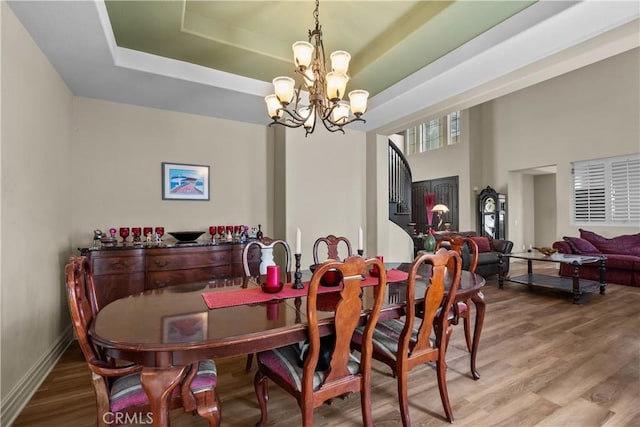 dining space with hardwood / wood-style flooring, a high ceiling, a tray ceiling, and a chandelier