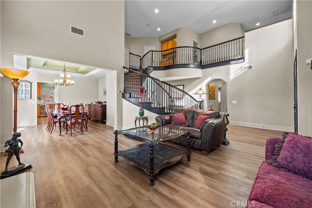 living room with a tray ceiling, light hardwood / wood-style flooring, a high ceiling, and an inviting chandelier