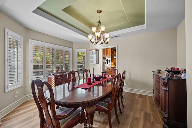 dining area featuring a raised ceiling, hardwood / wood-style flooring, and an inviting chandelier