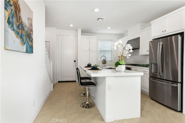 kitchen featuring white cabinetry, a kitchen bar, a center island with sink, stainless steel refrigerator with ice dispenser, and sink