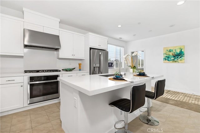 kitchen featuring appliances with stainless steel finishes, a kitchen island with sink, wall chimney exhaust hood, white cabinets, and sink