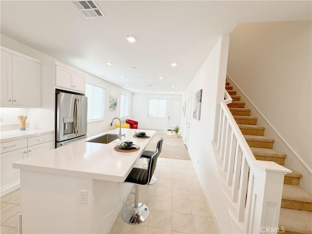 kitchen featuring a kitchen bar, sink, a kitchen island with sink, stainless steel fridge with ice dispenser, and white cabinets