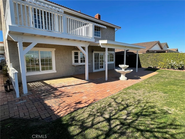 rear view of house featuring a patio, a balcony, fence, stucco siding, and a lawn