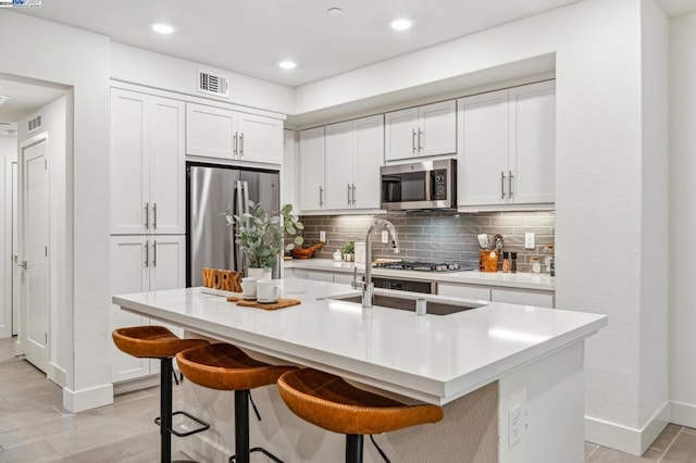 kitchen with a kitchen breakfast bar, white cabinetry, appliances with stainless steel finishes, and a center island with sink