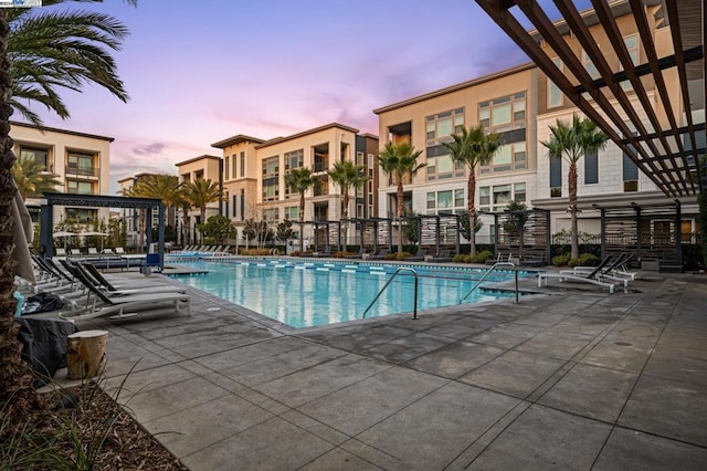 pool at dusk featuring a patio and a pergola