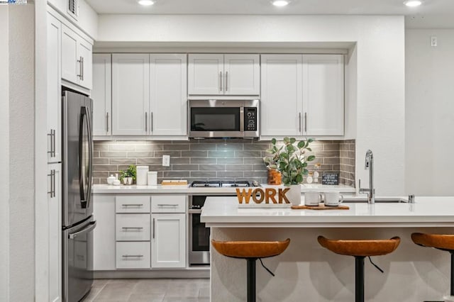 kitchen with white cabinetry, decorative backsplash, sink, a breakfast bar, and stainless steel appliances