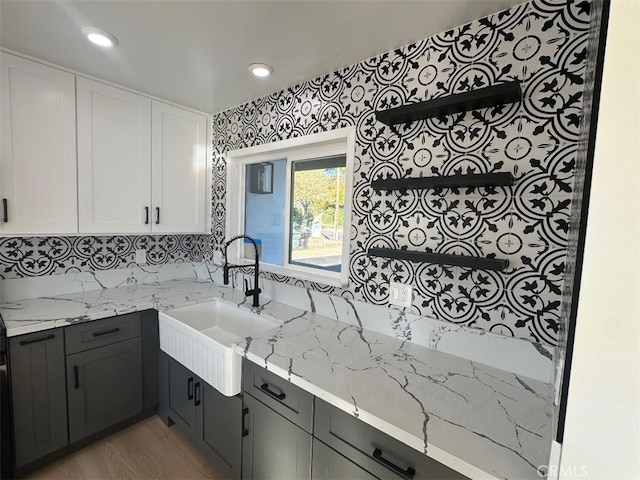 kitchen featuring light stone countertops, decorative backsplash, sink, light hardwood / wood-style flooring, and white cabinetry