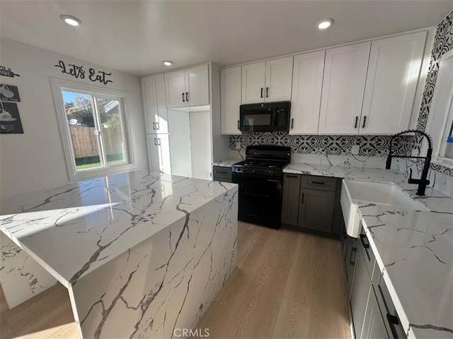 kitchen with light wood-type flooring, light stone counters, sink, black appliances, and white cabinets