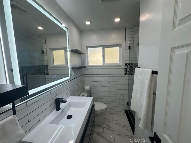 bathroom with vanity, toilet, tiled shower, and tile walls