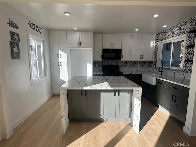 kitchen with sink, tasteful backsplash, light stone counters, light hardwood / wood-style floors, and black appliances