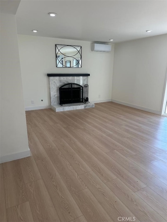 unfurnished living room with a wall unit AC, a tile fireplace, and light hardwood / wood-style flooring