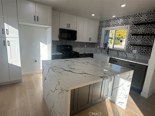 kitchen featuring a center island, black appliances, sink, light hardwood / wood-style flooring, and light stone counters