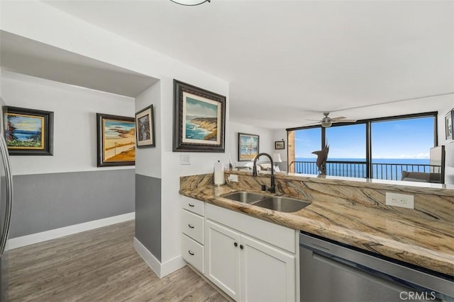 kitchen with white cabinetry, dishwasher, sink, light stone counters, and a water view