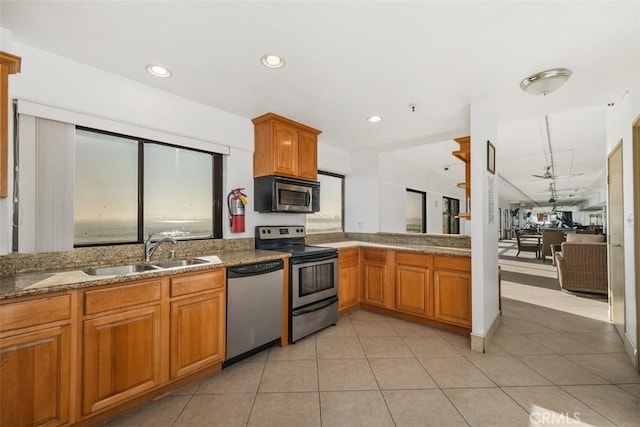 kitchen featuring stainless steel appliances, sink, light tile patterned floors, and light stone counters