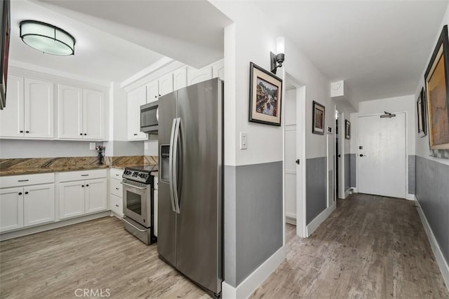 kitchen with appliances with stainless steel finishes, dark stone countertops, white cabinets, and light hardwood / wood-style floors