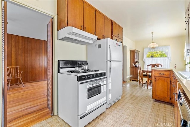 kitchen featuring hanging light fixtures, white appliances, wooden walls, and sink