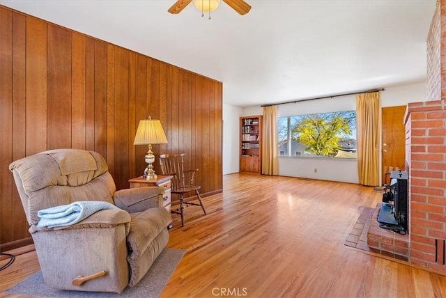 living area with light hardwood / wood-style flooring, ceiling fan, and wood walls