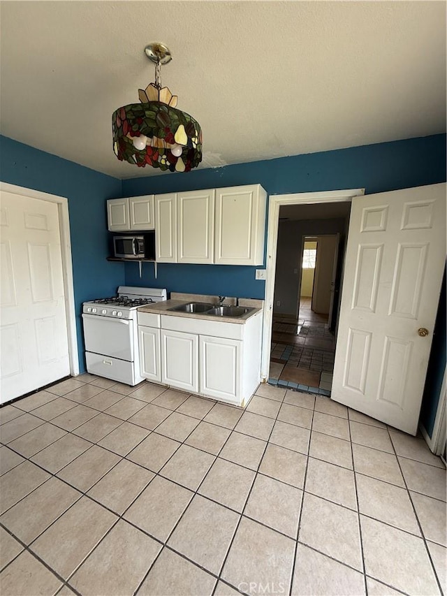 kitchen with white cabinets, light tile patterned floors, gas range gas stove, and sink