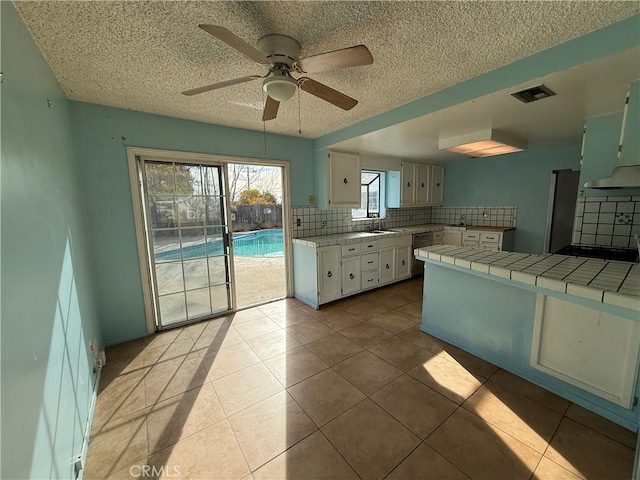 kitchen featuring decorative backsplash, ceiling fan, light tile patterned floors, tile countertops, and white cabinetry