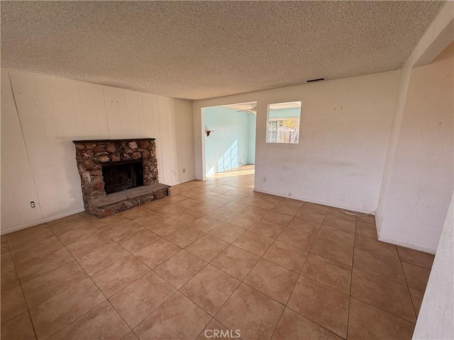 unfurnished living room featuring tile patterned floors, wooden walls, ceiling fan, a fireplace, and a textured ceiling