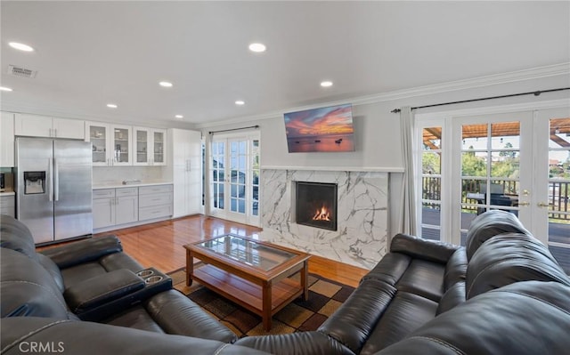 living room featuring a premium fireplace, french doors, light hardwood / wood-style floors, and ornamental molding