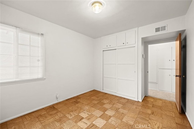 unfurnished bedroom featuring light parquet floors, a closet, and multiple windows