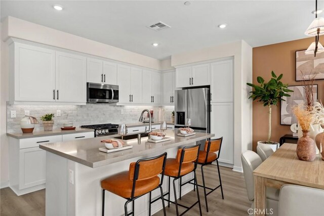 kitchen with stainless steel appliances, a kitchen island with sink, a kitchen breakfast bar, pendant lighting, and white cabinets