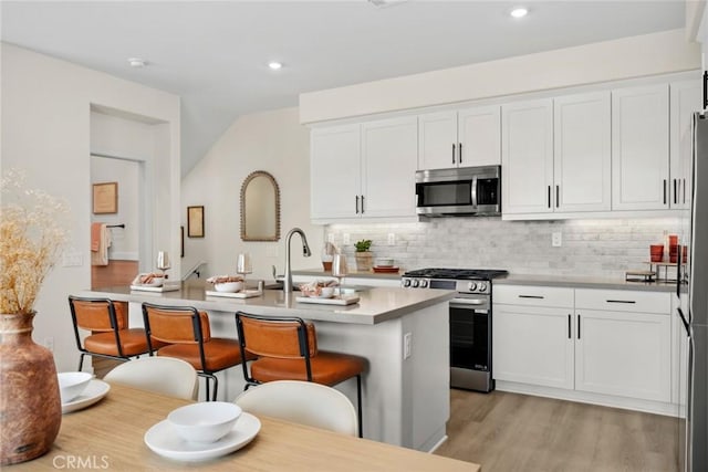 kitchen with white cabinets, appliances with stainless steel finishes, backsplash, a kitchen island with sink, and a breakfast bar area