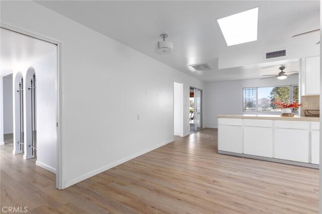 kitchen featuring light hardwood / wood-style flooring, ceiling fan, backsplash, white cabinetry, and a skylight