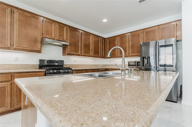 kitchen with light stone countertops, appliances with stainless steel finishes, a center island with sink, and sink