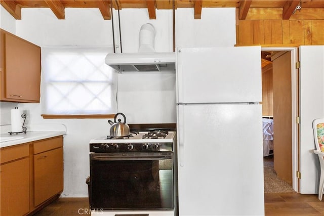 kitchen with gas stove, ventilation hood, white refrigerator, beamed ceiling, and hardwood / wood-style floors