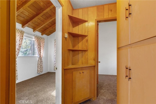 hallway featuring lofted ceiling with beams, dark carpet, wooden ceiling, and wood walls