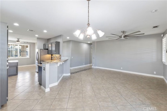 kitchen with kitchen peninsula, light stone counters, light tile patterned floors, and ceiling fan with notable chandelier