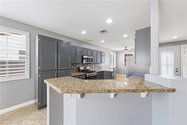 kitchen with a kitchen breakfast bar, kitchen peninsula, gray cabinetry, and stainless steel appliances