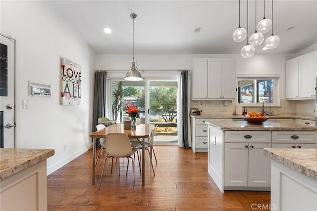 kitchen with light stone counters, white cabinetry, dark wood-type flooring, and a wealth of natural light