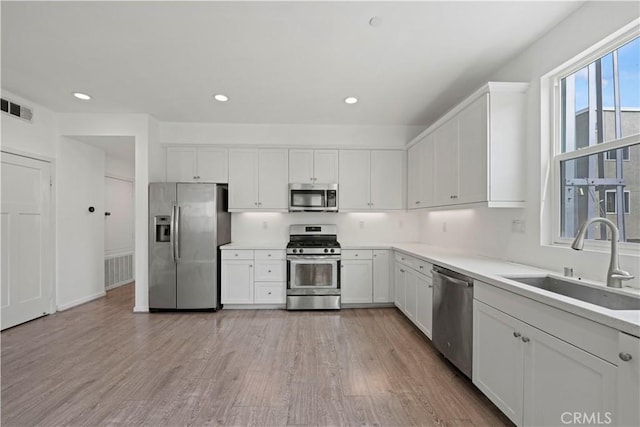 kitchen with stainless steel appliances, light hardwood / wood-style flooring, white cabinetry, and sink