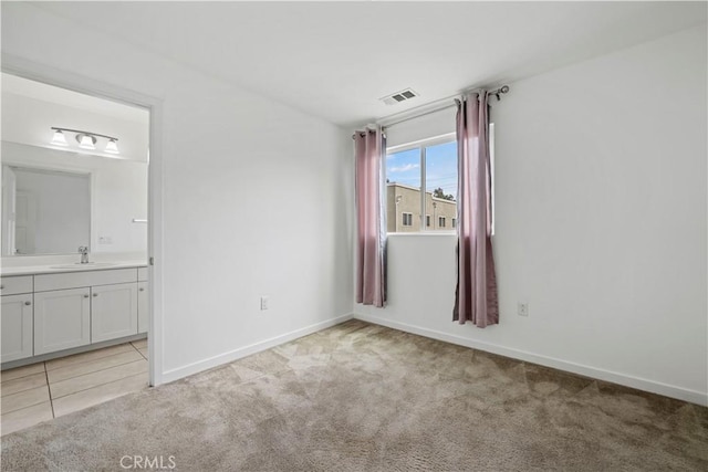 unfurnished bedroom with light colored carpet, ensuite bath, and sink