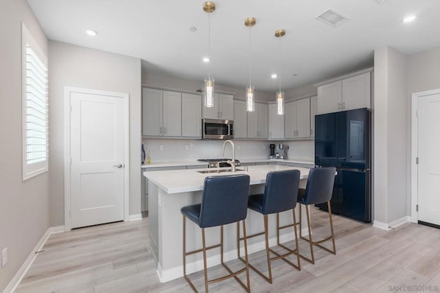 kitchen with gray cabinets, stainless steel appliances, tasteful backsplash, a kitchen island with sink, and sink