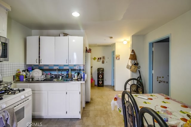 kitchen with white gas range, decorative backsplash, and white cabinetry