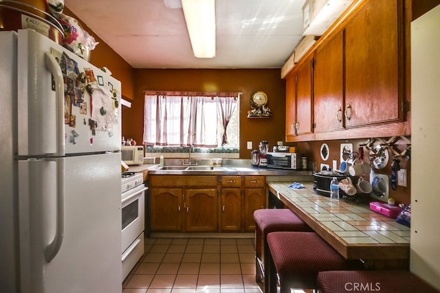 kitchen featuring tile counters, sink, light tile patterned floors, and white appliances