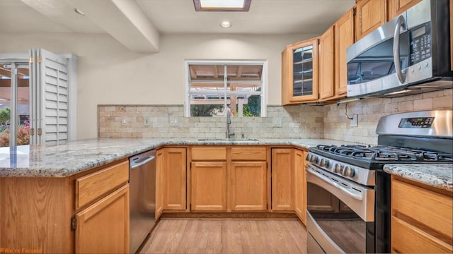 kitchen featuring kitchen peninsula, appliances with stainless steel finishes, light wood-type flooring, light stone counters, and sink