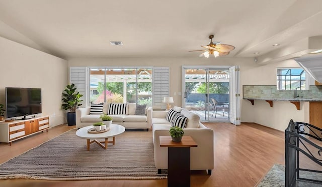 living room featuring ceiling fan, light wood-type flooring, sink, and a wealth of natural light