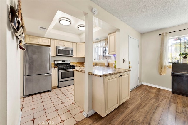 kitchen with light stone counters, cream cabinets, light hardwood / wood-style floors, a textured ceiling, and appliances with stainless steel finishes