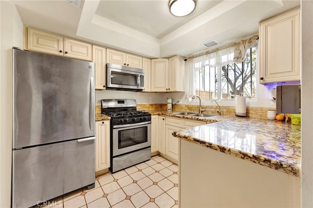 kitchen with light stone countertops, appliances with stainless steel finishes, a raised ceiling, sink, and cream cabinetry