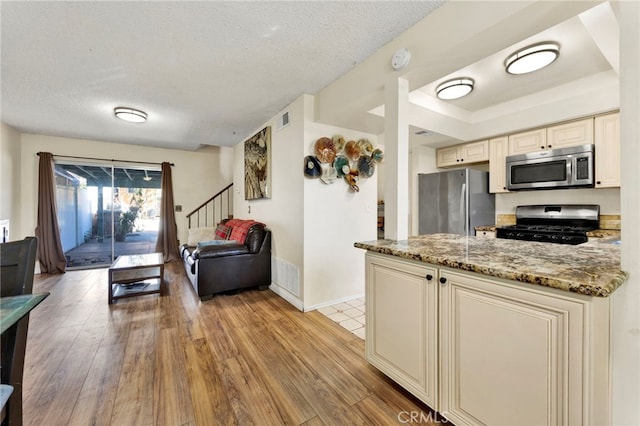 kitchen featuring light hardwood / wood-style flooring, light stone countertops, a textured ceiling, cream cabinetry, and stainless steel appliances