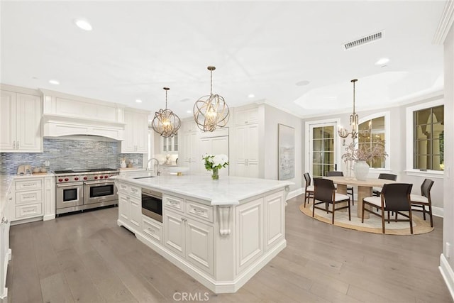 kitchen featuring pendant lighting, stainless steel appliances, light hardwood / wood-style flooring, and a kitchen island with sink