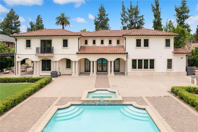 back of property featuring a patio, a balcony, and a pool with hot tub