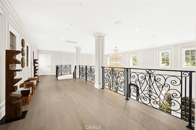 hall featuring a chandelier, light wood-type flooring, ornamental molding, and decorative columns