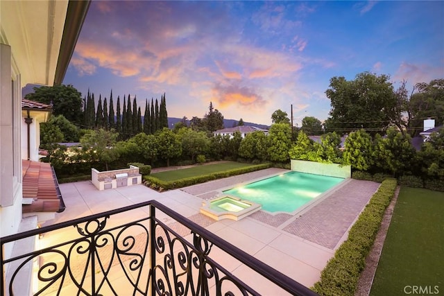 pool at dusk with an in ground hot tub and a patio area