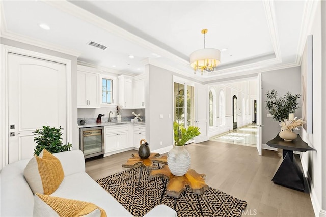 living room with light hardwood / wood-style floors, crown molding, sink, and wine cooler